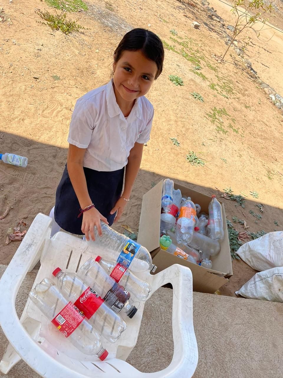 Child arranging plastic bottles on a white table outdoors in a sandy area