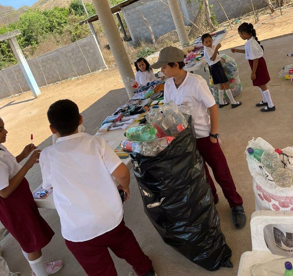 Children in uniforms gather around tables outdoors, sorting and handling bags of supplies.