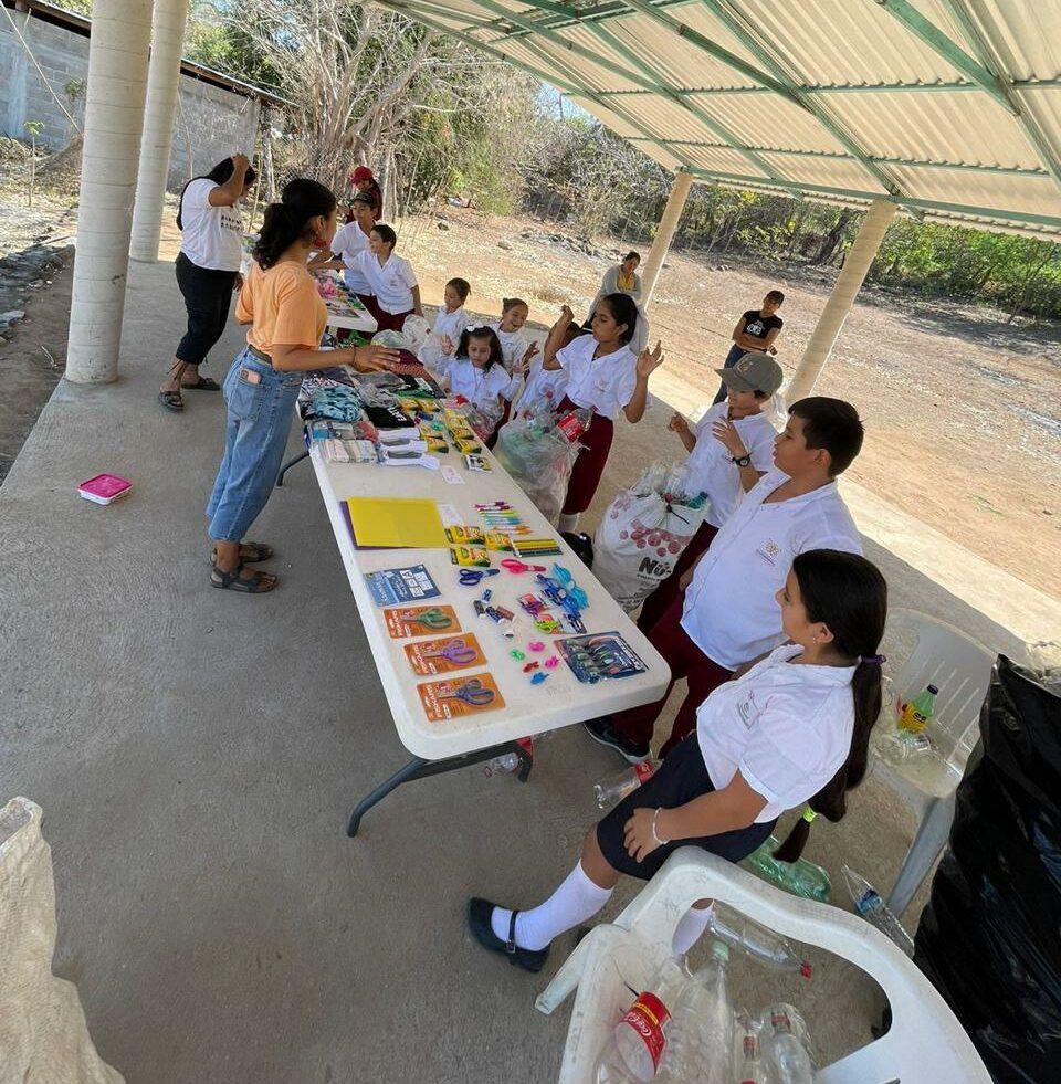 Children seated at a table outdoors, doing a colorful craft activity under a shaded pavilion.