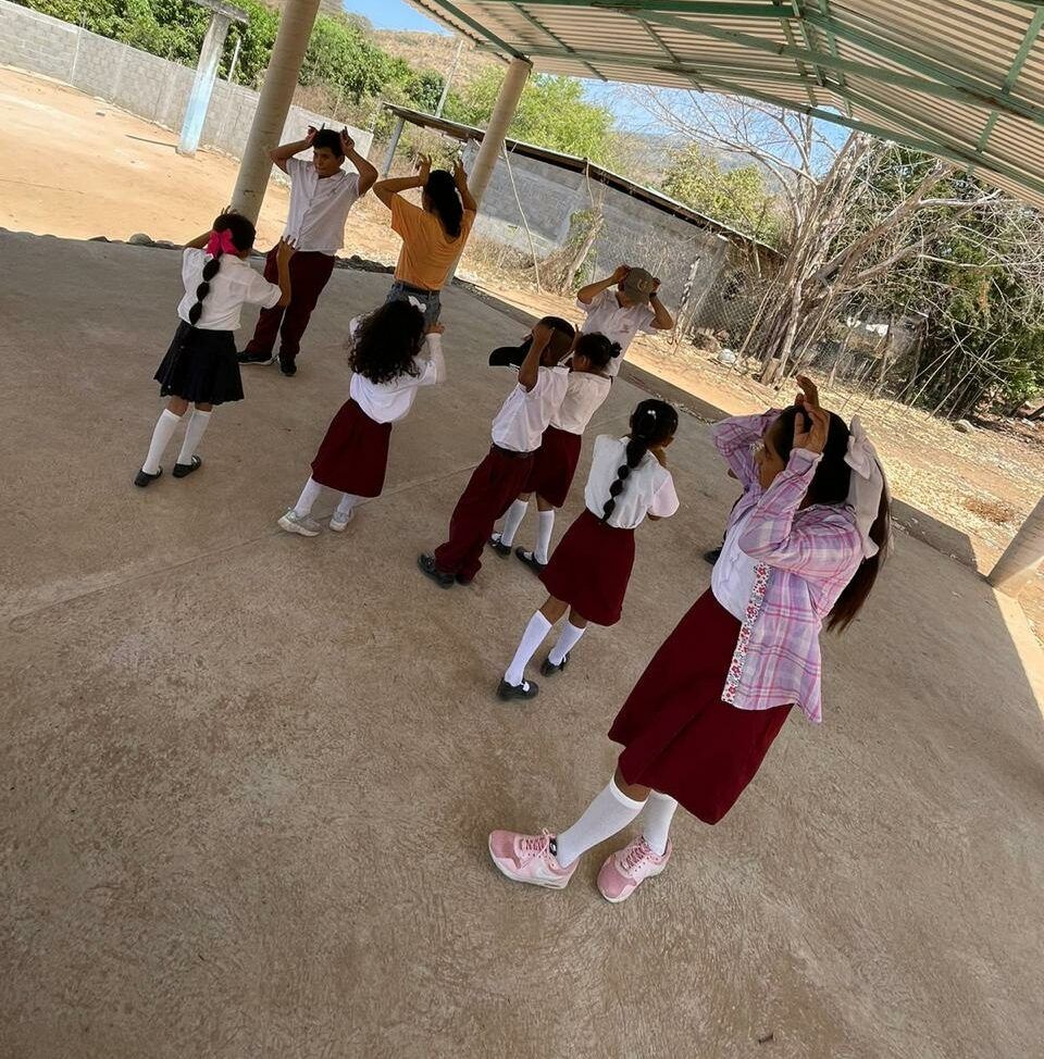 Children in school uniforms standing in a circle doing an outdoor activity under a shaded pavilion