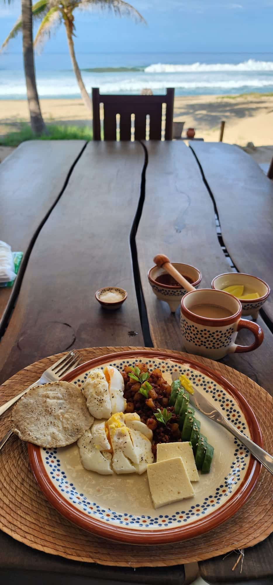 Beachfront breakfast on a wooden table with eggs, toast, fruit, coffee, and ocean view
