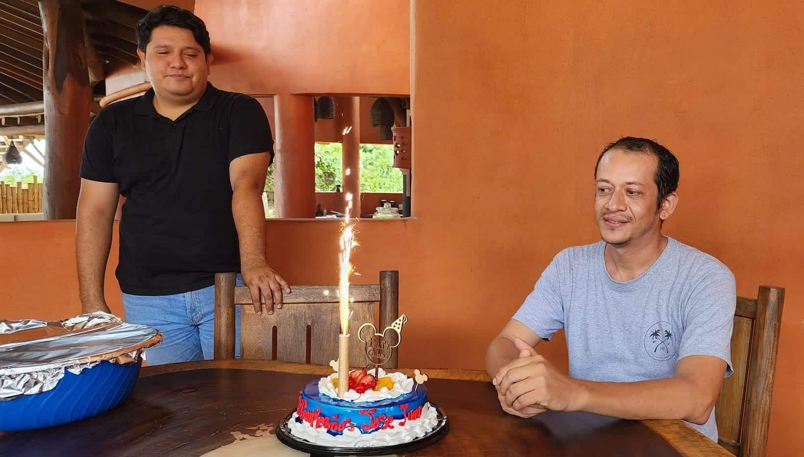 Two people at a table with a birthday cake and candles in a warm indoor setting
