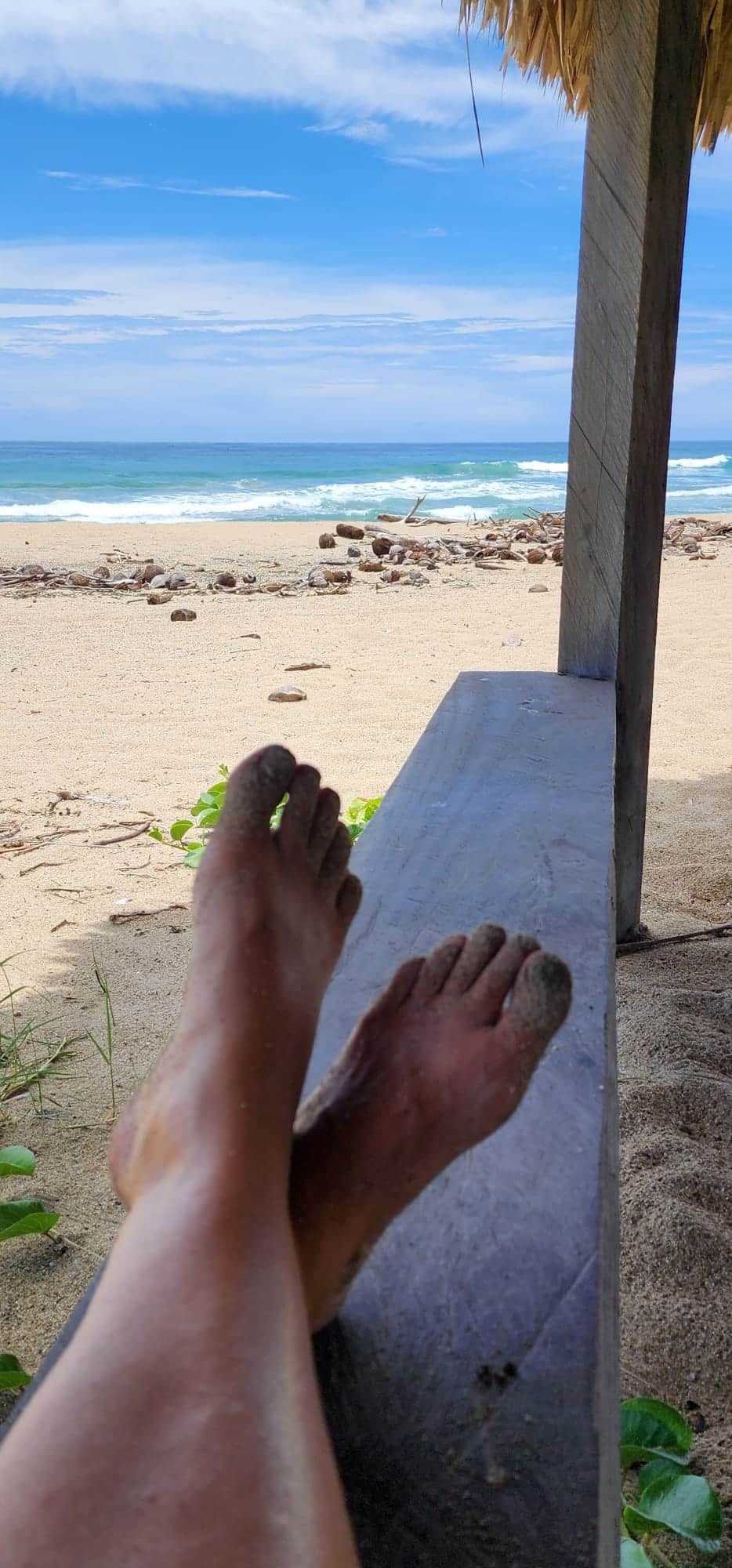 Relaxing feet on a shaded bench overlooking a sunny beach and blue ocean