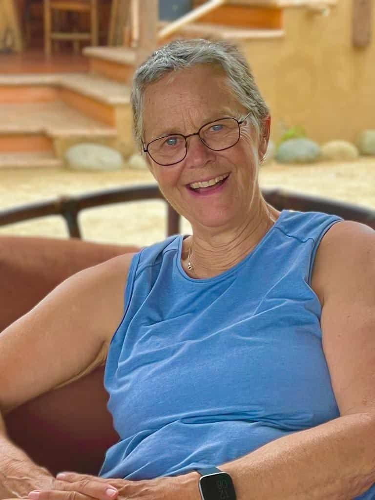 Smiling person in glasses and blue shirt sitting on a porch chair