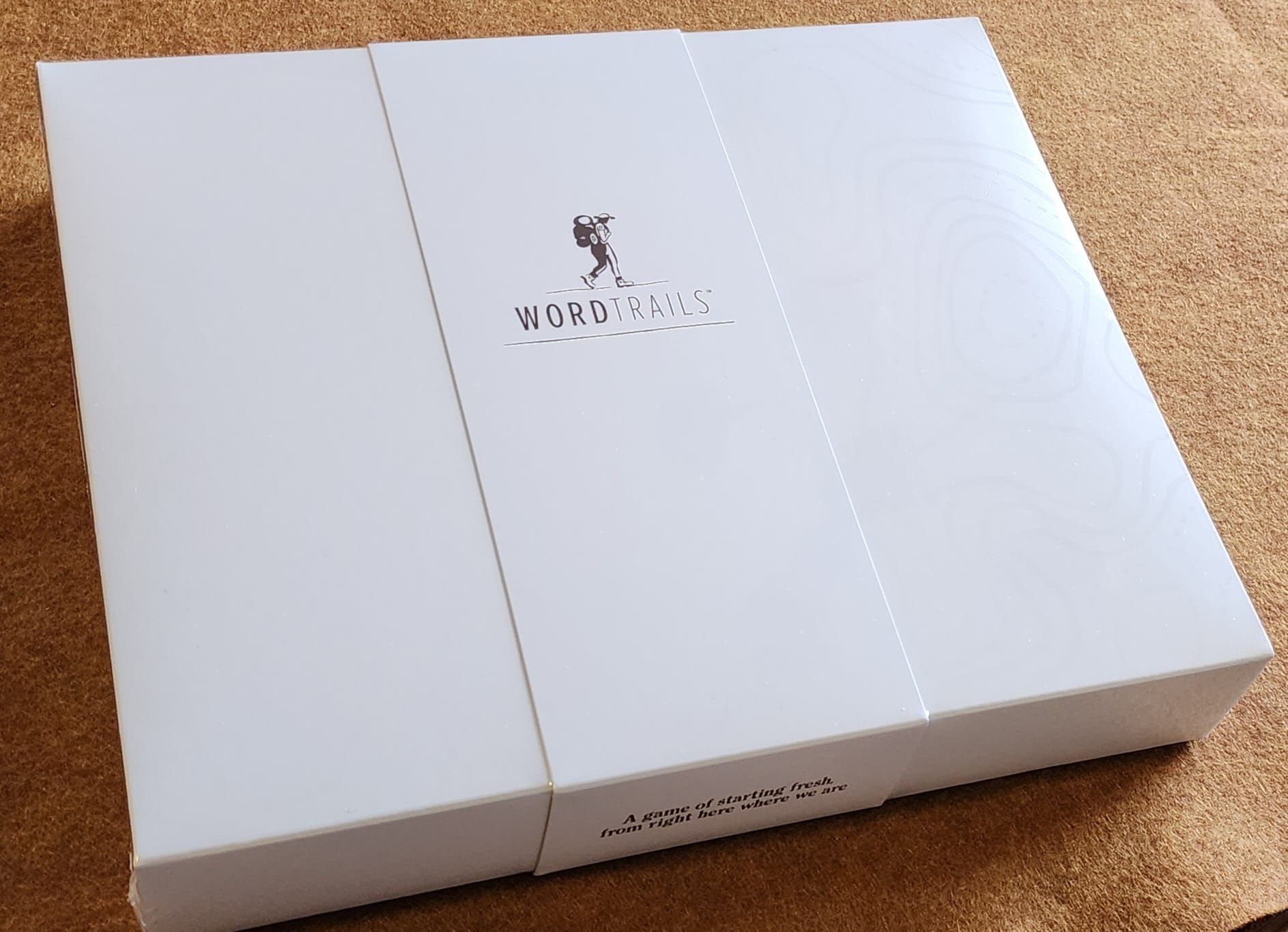 White perfume box with a logo on top, shown closed on a cork surface.