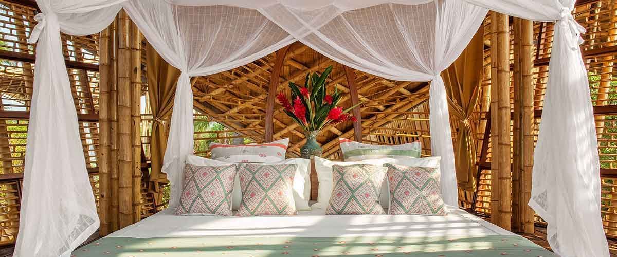 Beach cabana bed with white canopy, woven bamboo walls, and tropical flowers at the headboard