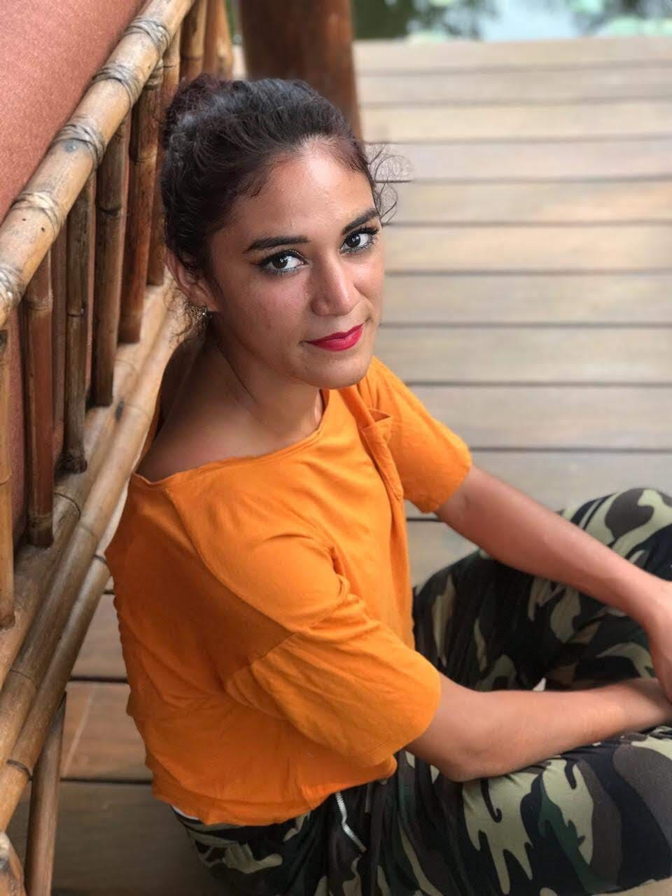 Woman in orange top sitting on wooden stairs, looking at the camera.