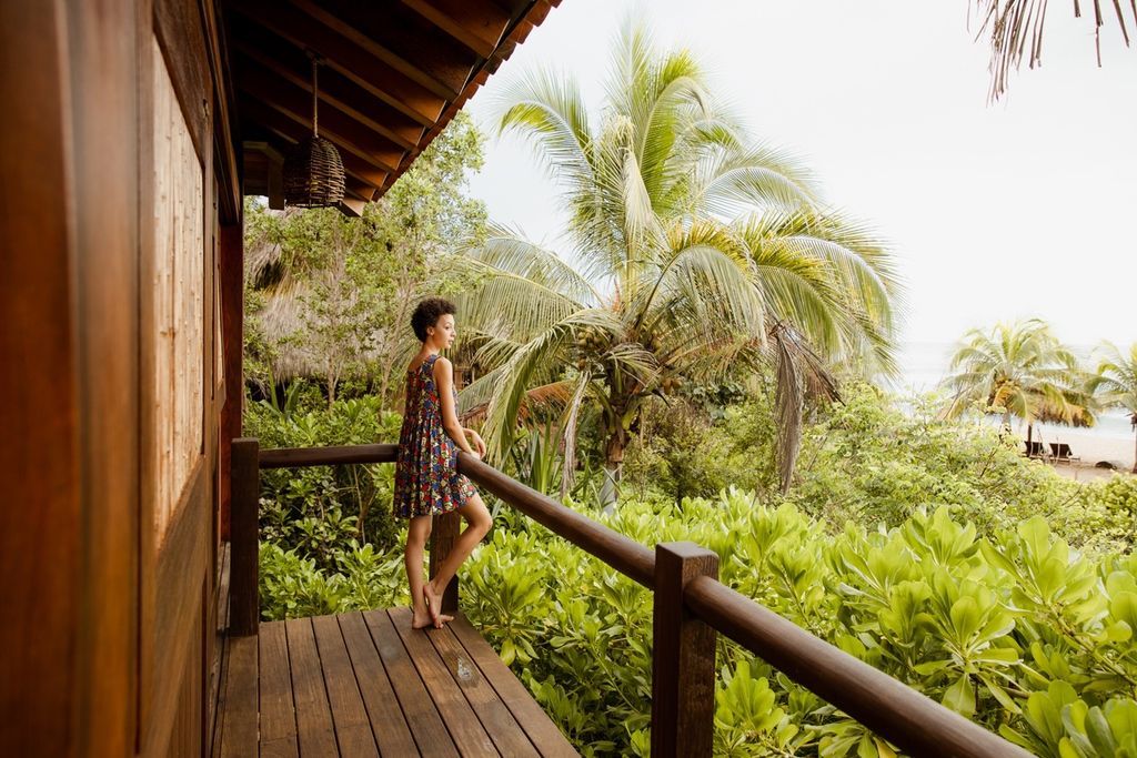 Person standing on a wooden balcony overlooking lush tropical greenery and palm trees