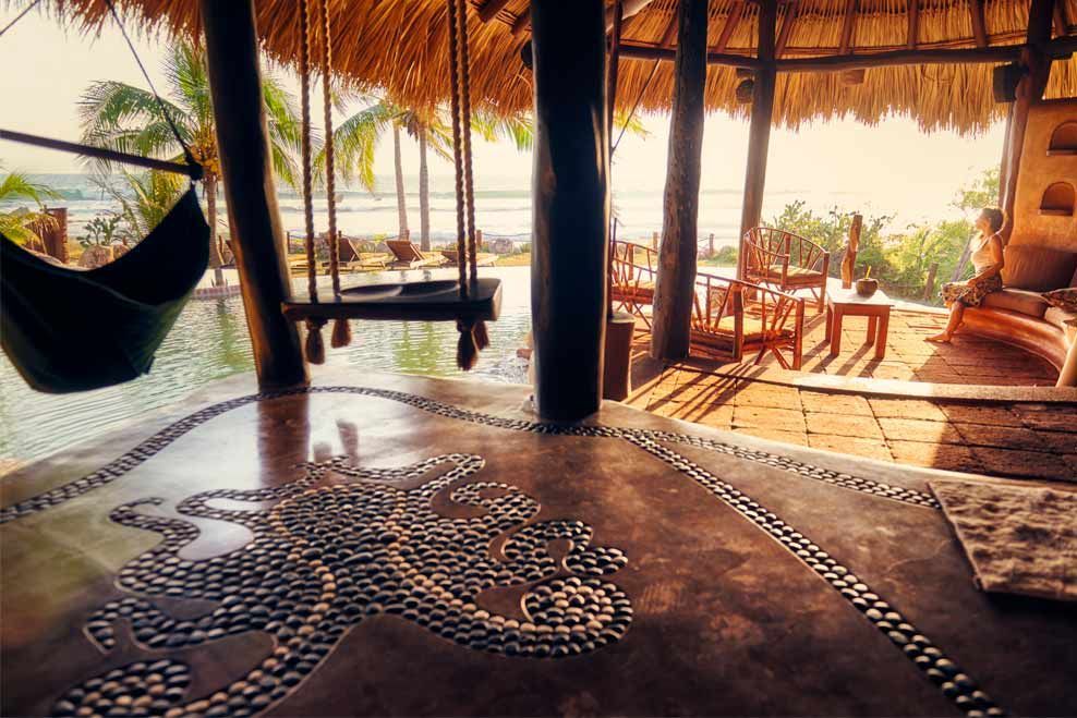 Rustic beach hut interior with hammock, wooden deck, and warm sunset light over the ocean