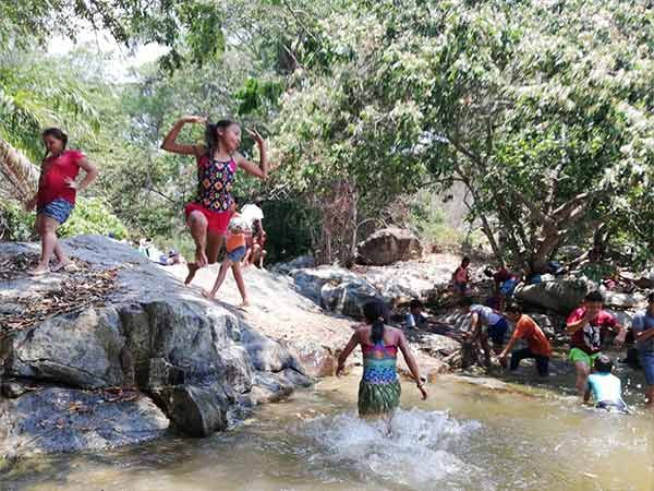 People splashing and climbing on rocks in a shallow forest stream