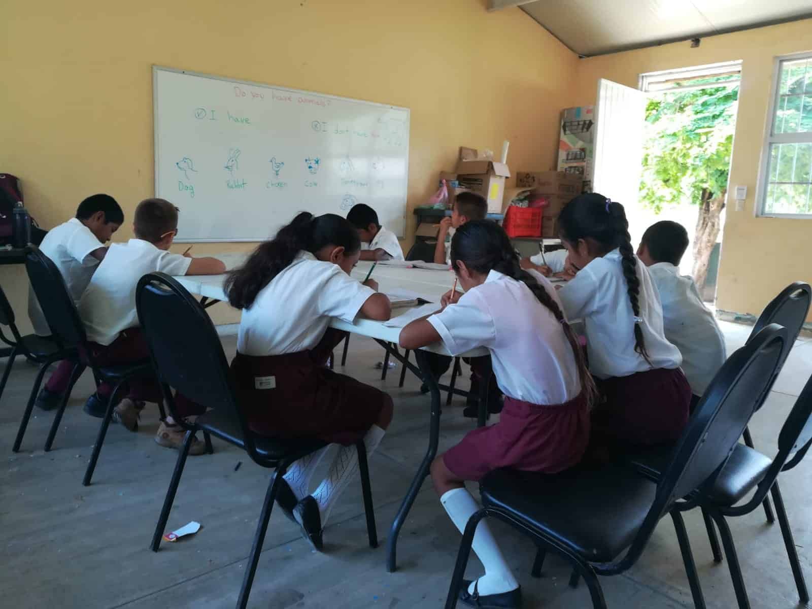 Students seated around tables in a classroom, working together on a group activity near a whiteboard.
