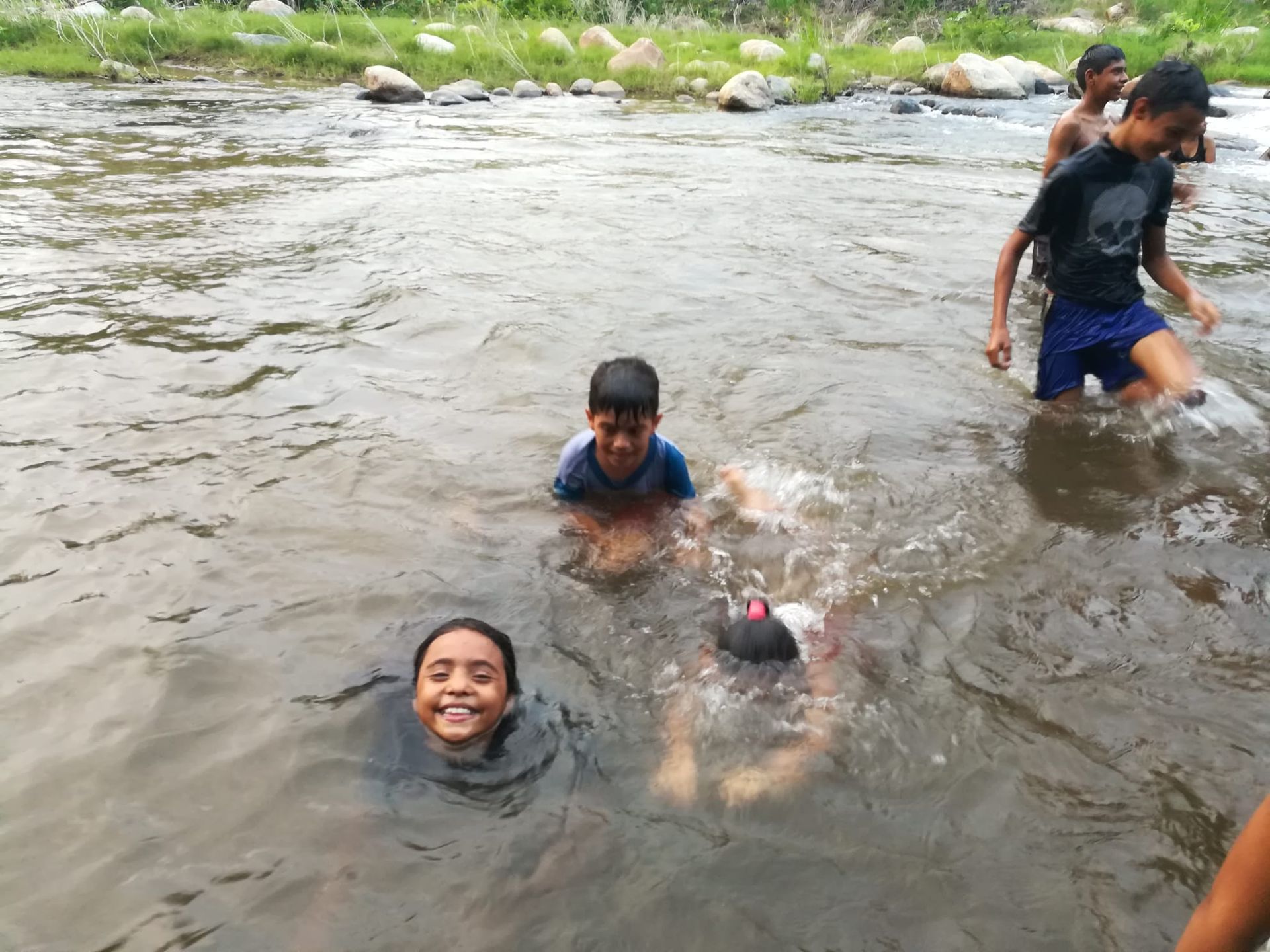 People swimming and splashing in a shallow river near the bank.