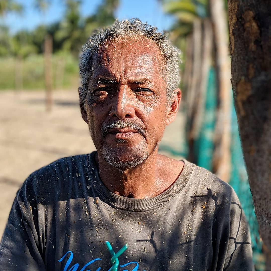 Portrait of a man outdoors in sunlight, wearing a dark T-shirt against a blurred beach background
