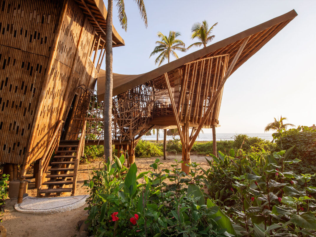 Rustic bamboo cabins with staircases and lush tropical plants under a warm sunset sky