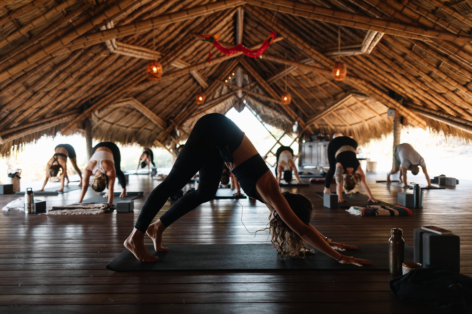 People doing yoga stretches on wooden floor in a thatched-roof studio