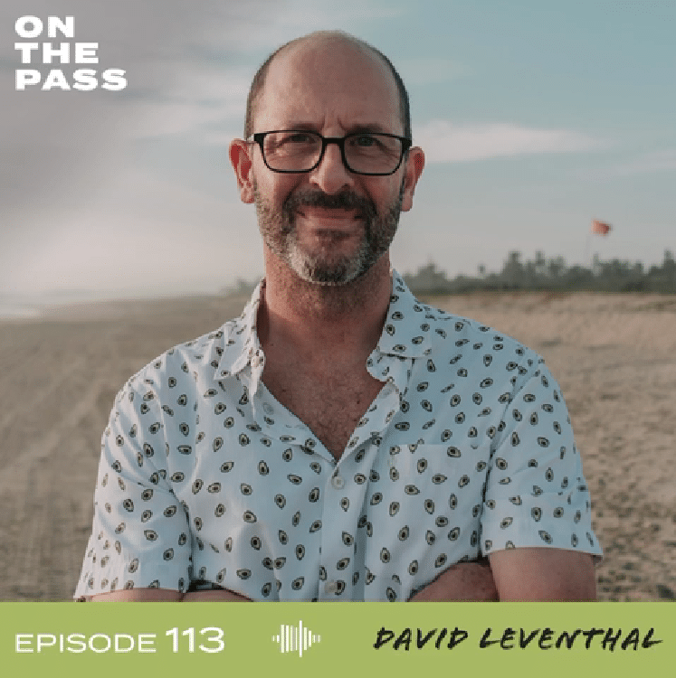 David Leventhal poses on a beach in a white patterned shirt for the On the Pass podcast, episode 113.