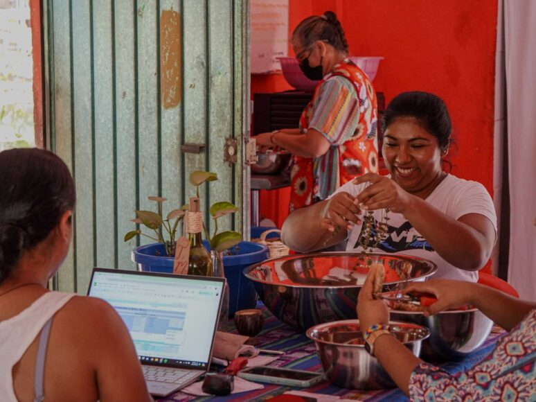 People sharing food at a table in a red room, with a laptop open in the foreground.