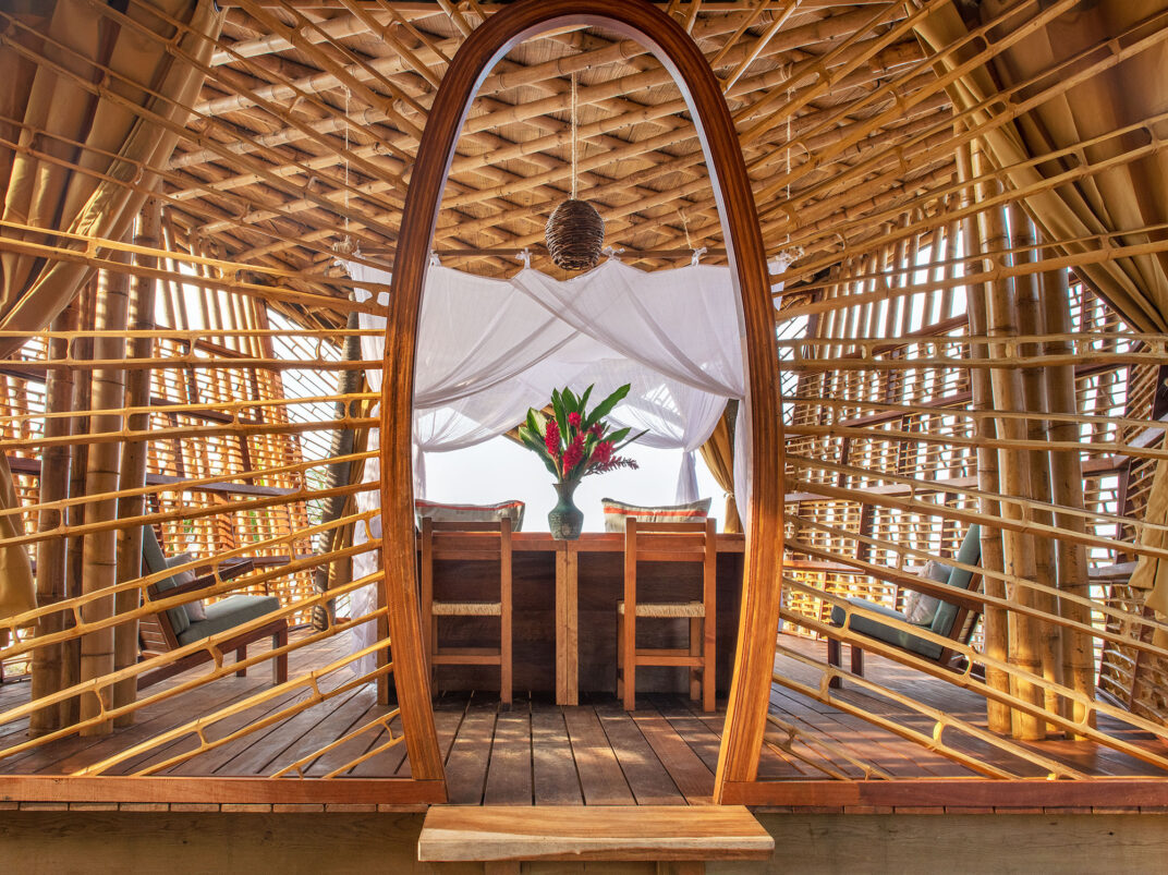 Wooden bamboo cabin interior with arched doorway, hanging lantern, and table set with flowers by a bright window