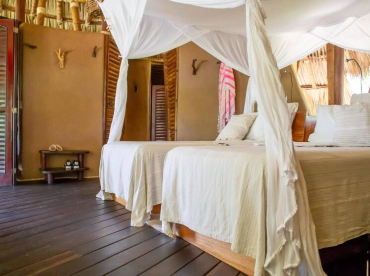 A hotel room with two beds, draped in white canopy netting, set against rustic brown walls and a wooden floor.