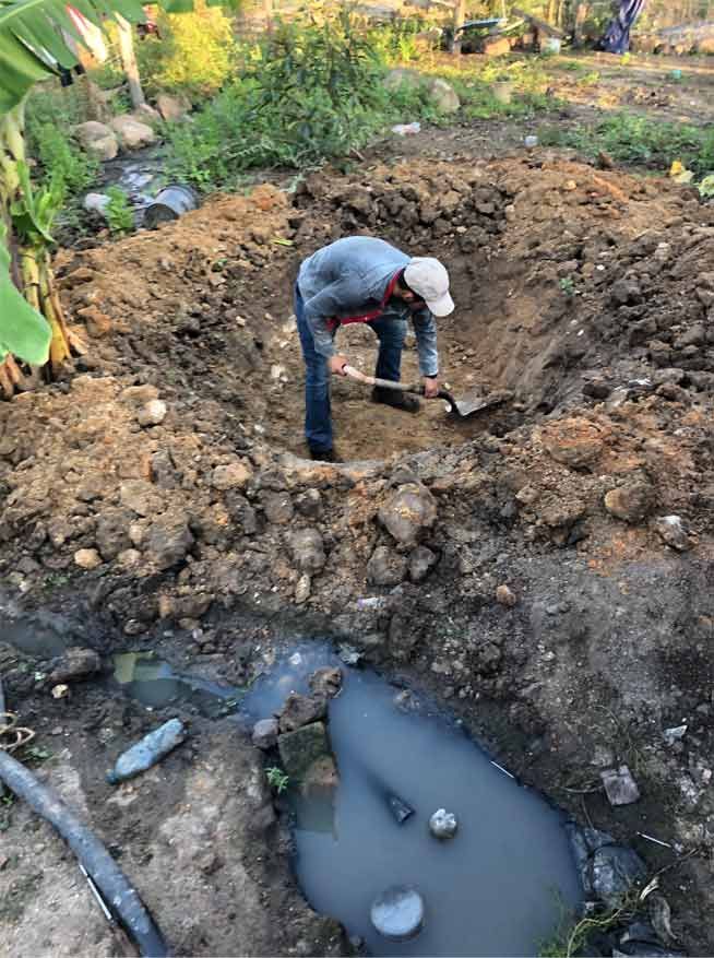 Person digging in a muddy pit beside a small pool of dark water outdoors