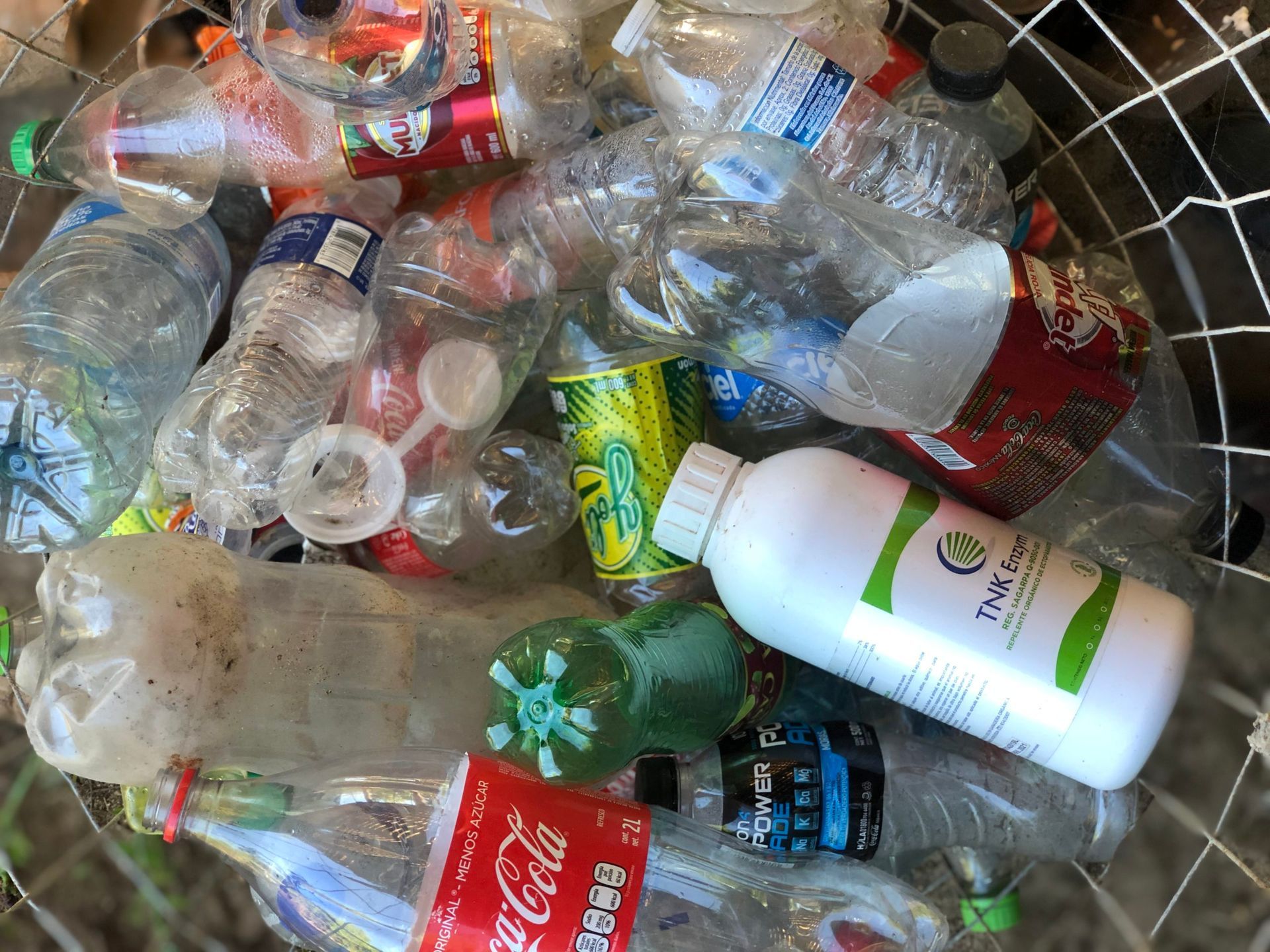 Plastic bottles and cans piled in a wire recycling bin