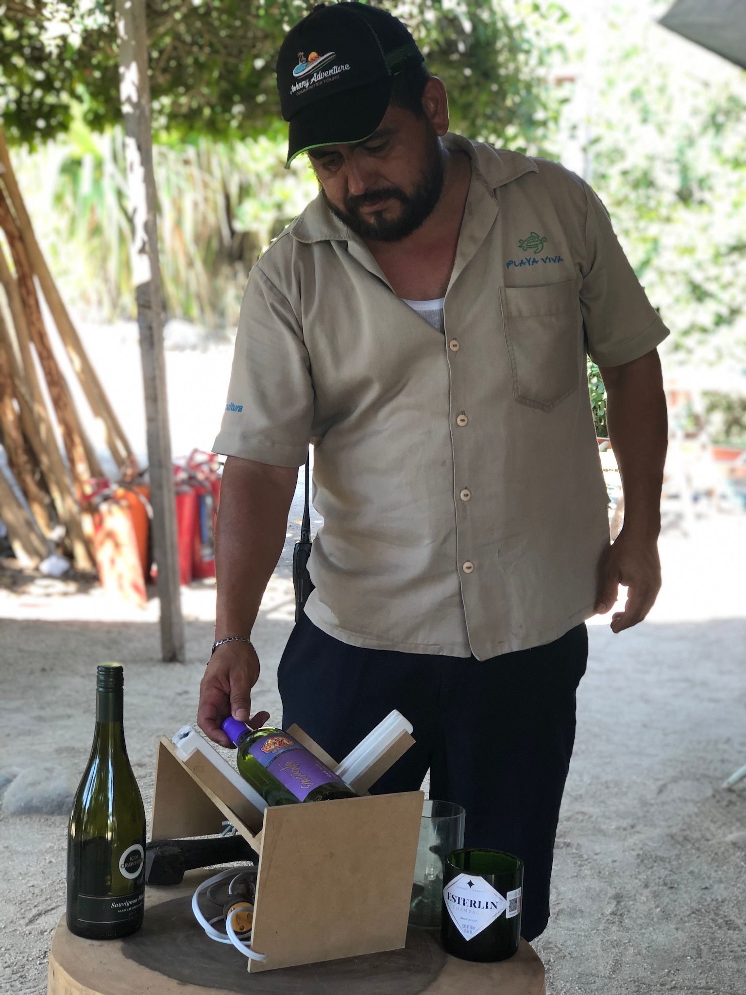 Man standing outdoors beside a box of bottles and supplies on a table