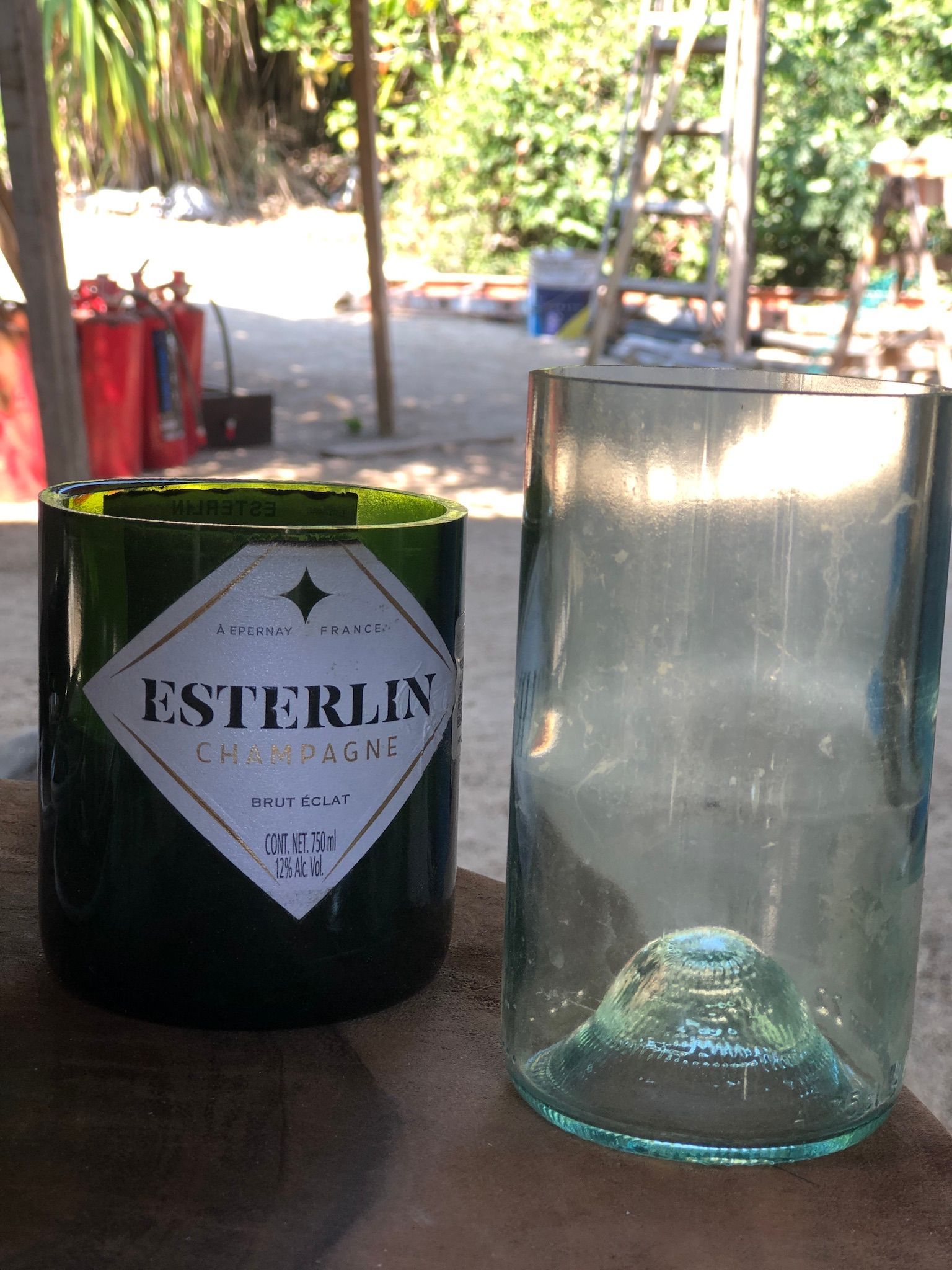 Green bottle and clear glass tumbler on a table outdoors, with a red Esterlin wine label visible.