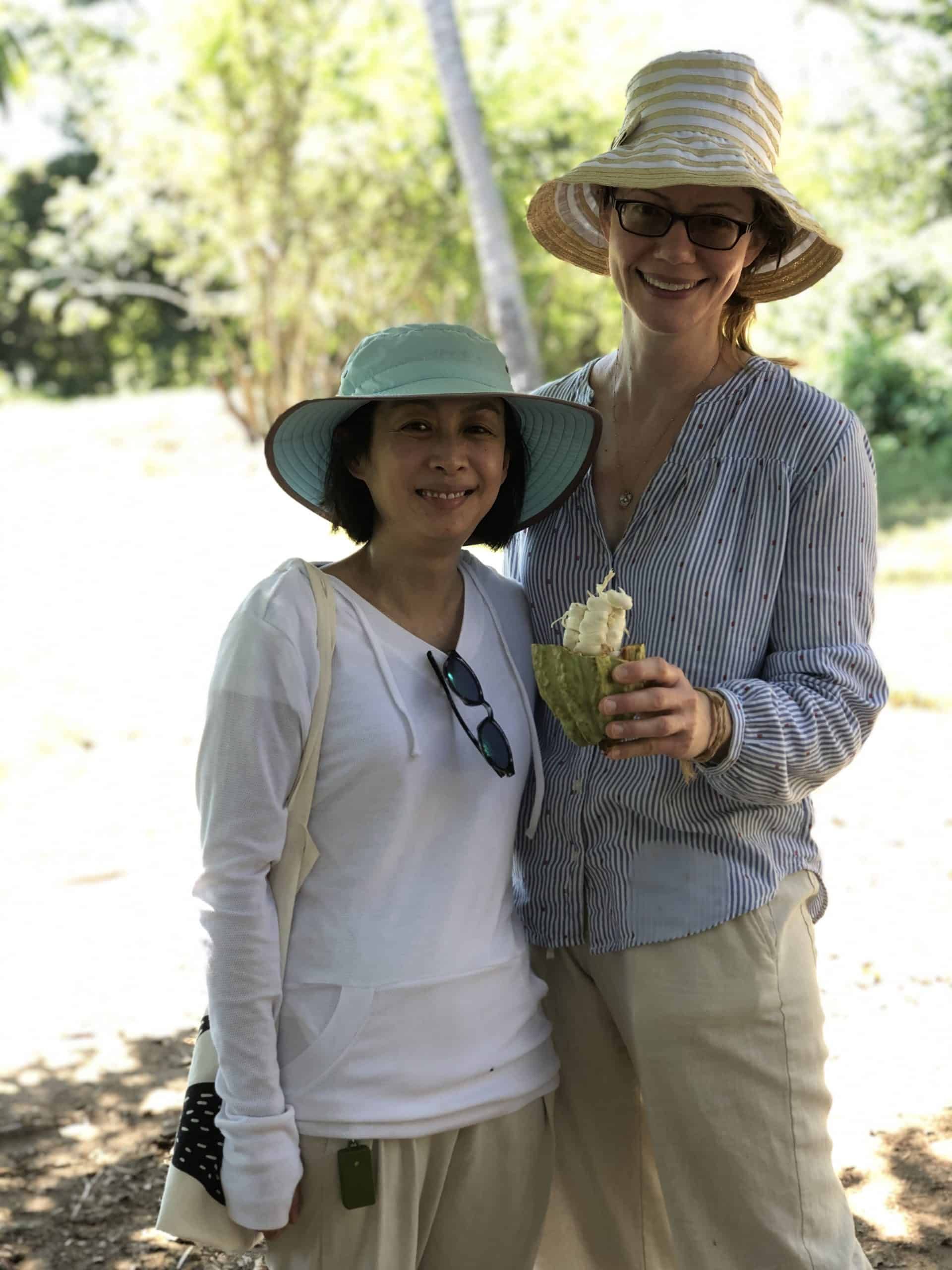 Two smiling people in sun hats outdoors, one holding a drink, in bright sunlight