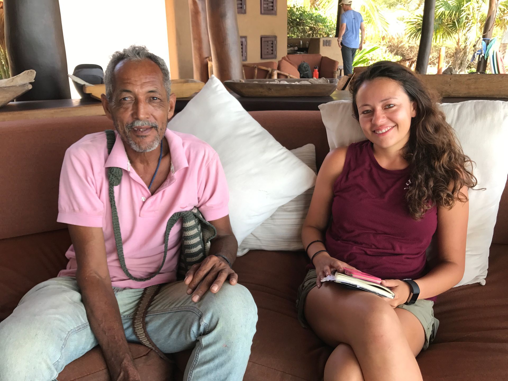 Two people sitting on a couch, smiling, in a casual indoor setting.