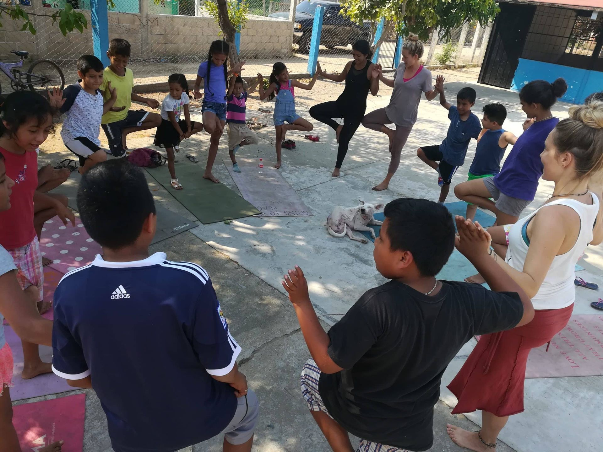 Children exercising in a circle outdoors on a concrete court, with an instructor demonstrating in the center.