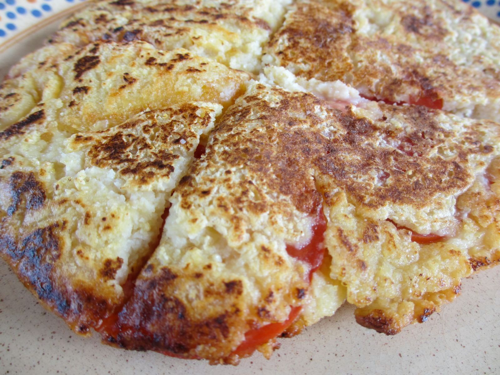 Close-up of a browned cheese omelet on a plate, with a slice cut out.