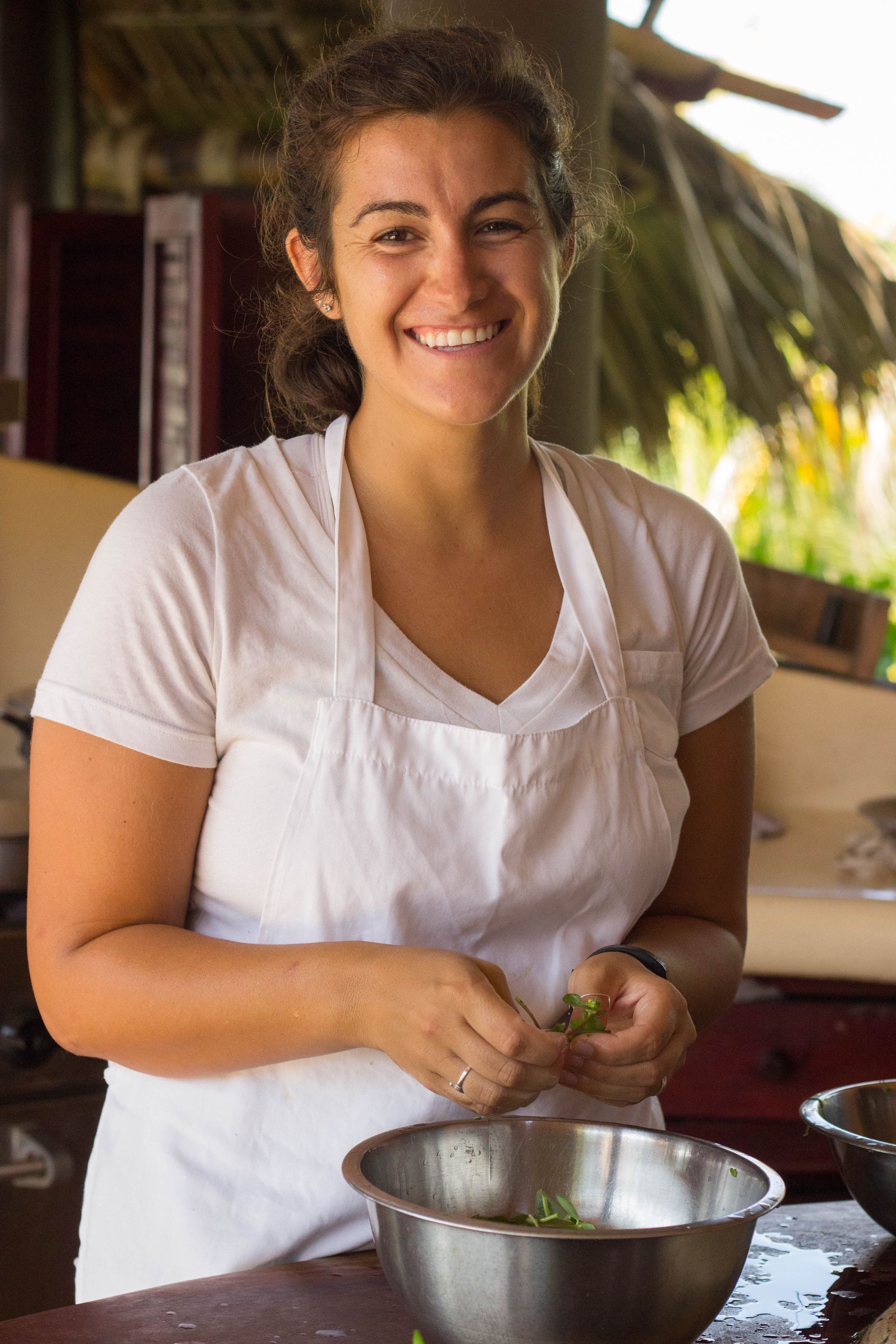 Smiling person in a white shirt and apron mixing ingredients in a bowl in a kitchen