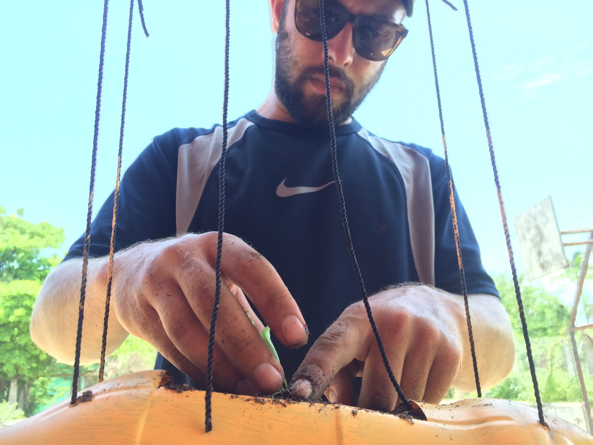 Person wearing sunglasses and gloves works on a black wire structure outdoors in bright sunlight
