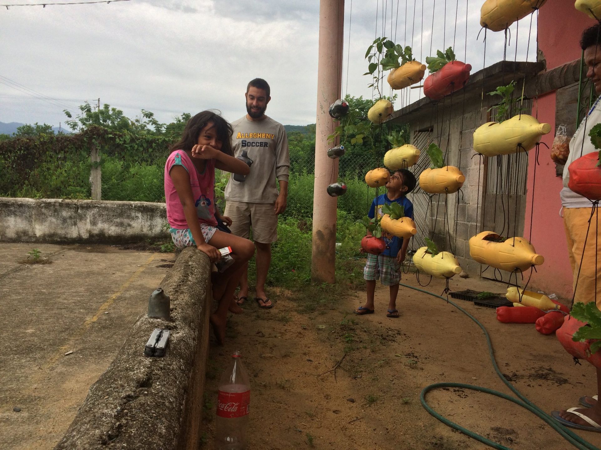 Two people by a fence with hanging yellow and red pots in a garden area