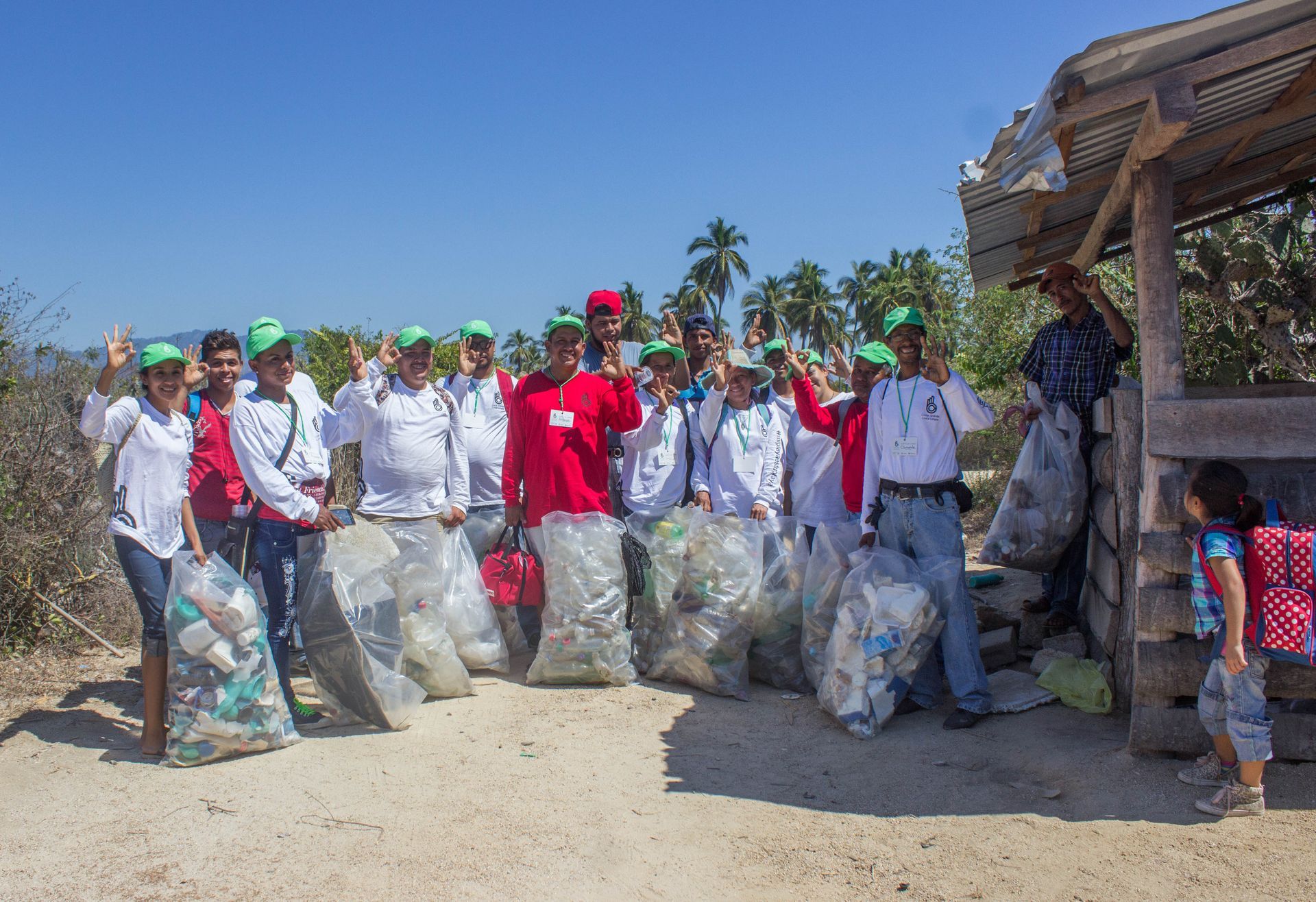 Group of people holding trash bags during a community cleanup outdoors on a sunny day