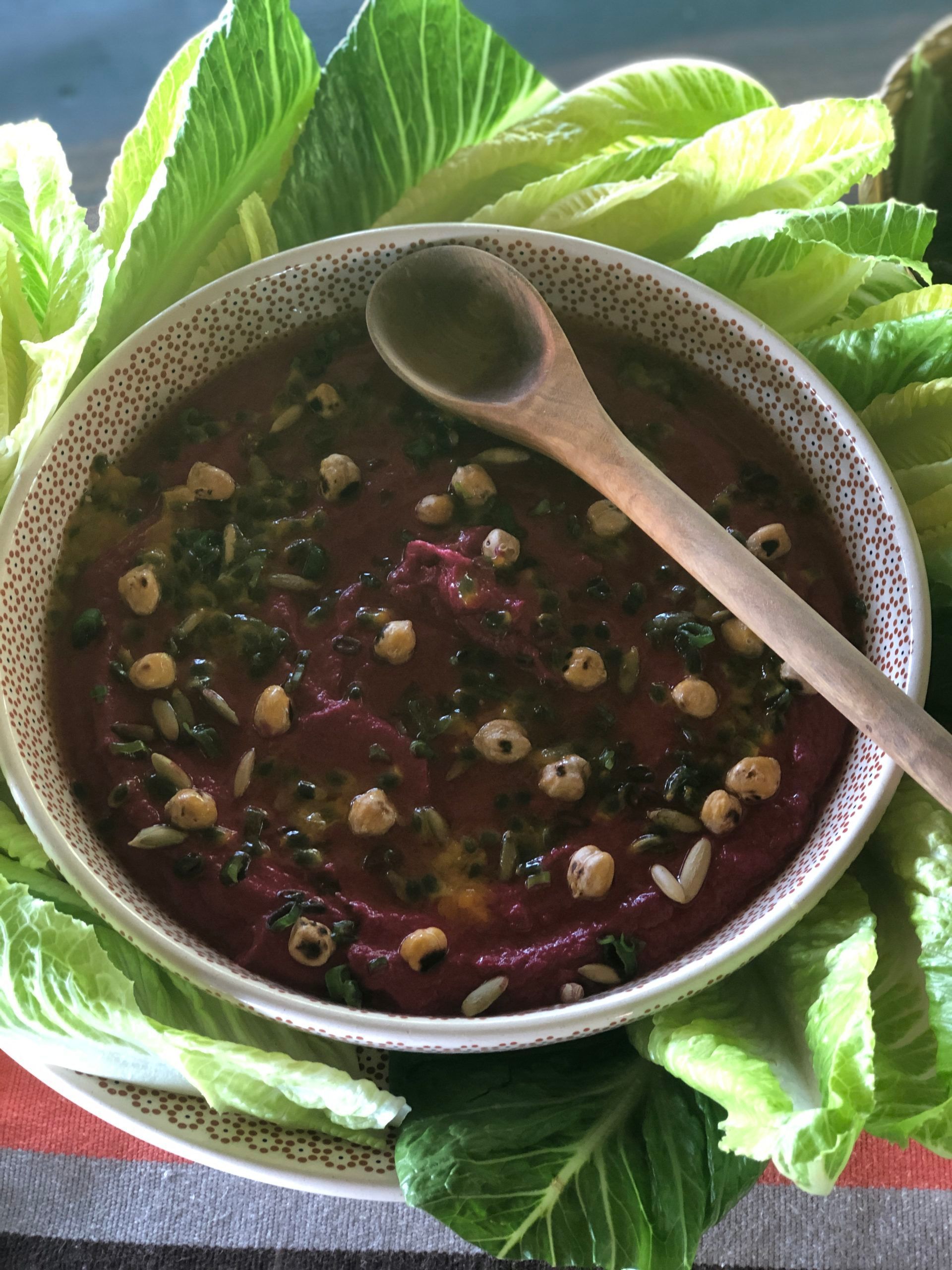 Bowl of dark soup with beans and herbs, served on green lettuce leaves with a wooden spoon