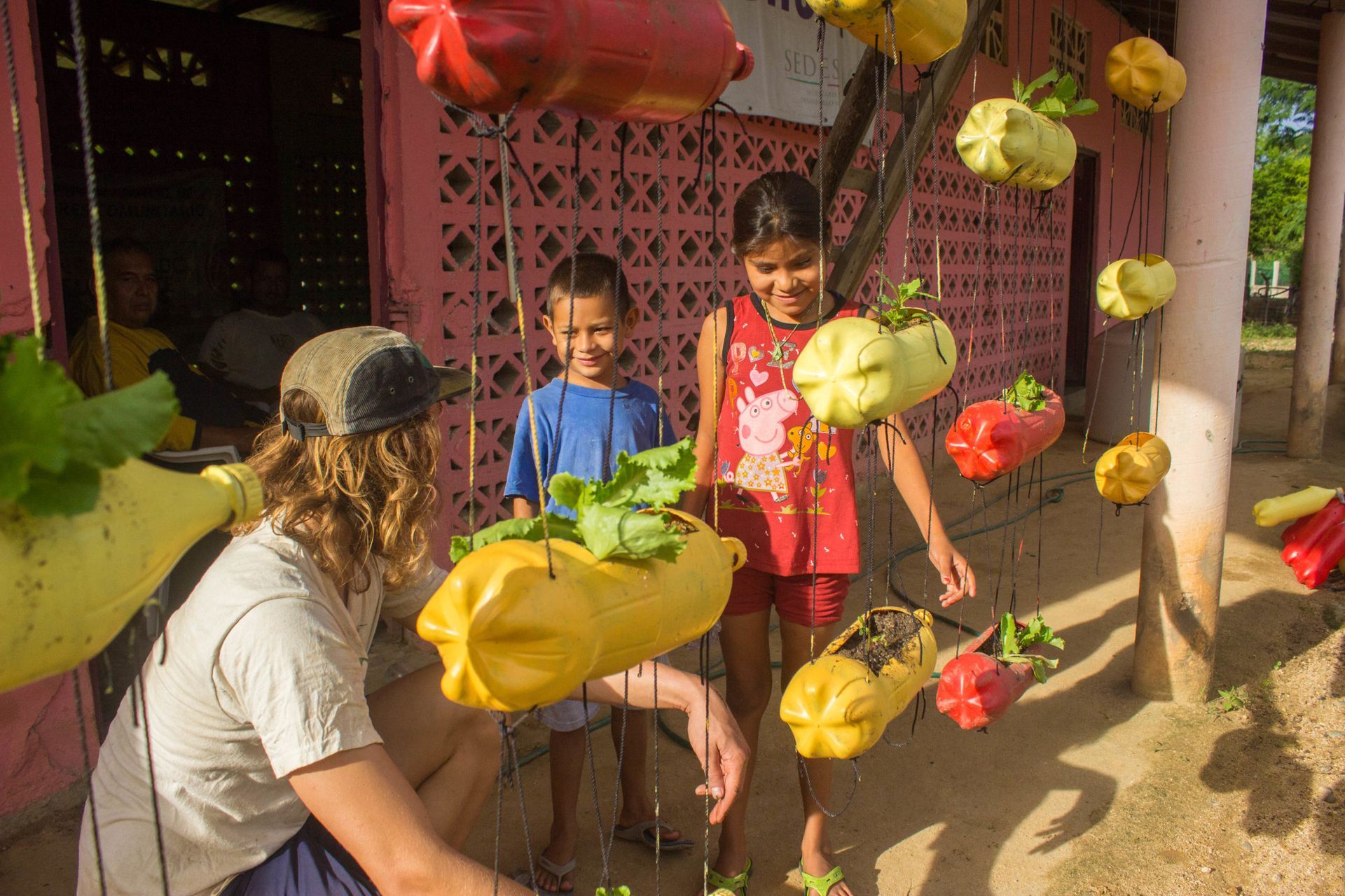 Children playing with hanging colorful bean bags outdoors near a building.