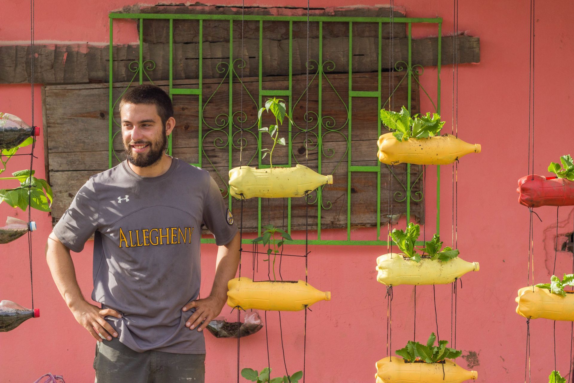 Man standing by a red wall with hanging yellow and red planter pots and green plants