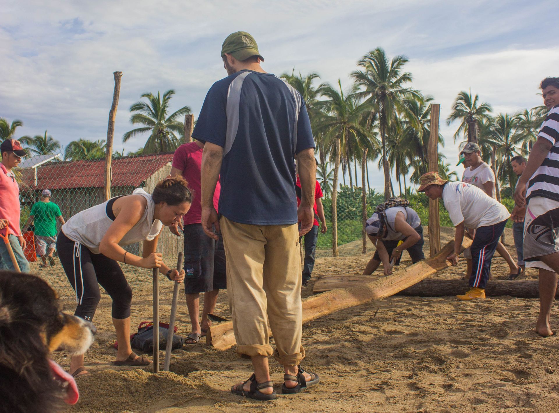 People shoveling dirt at a community work site with palm trees and houses in the background