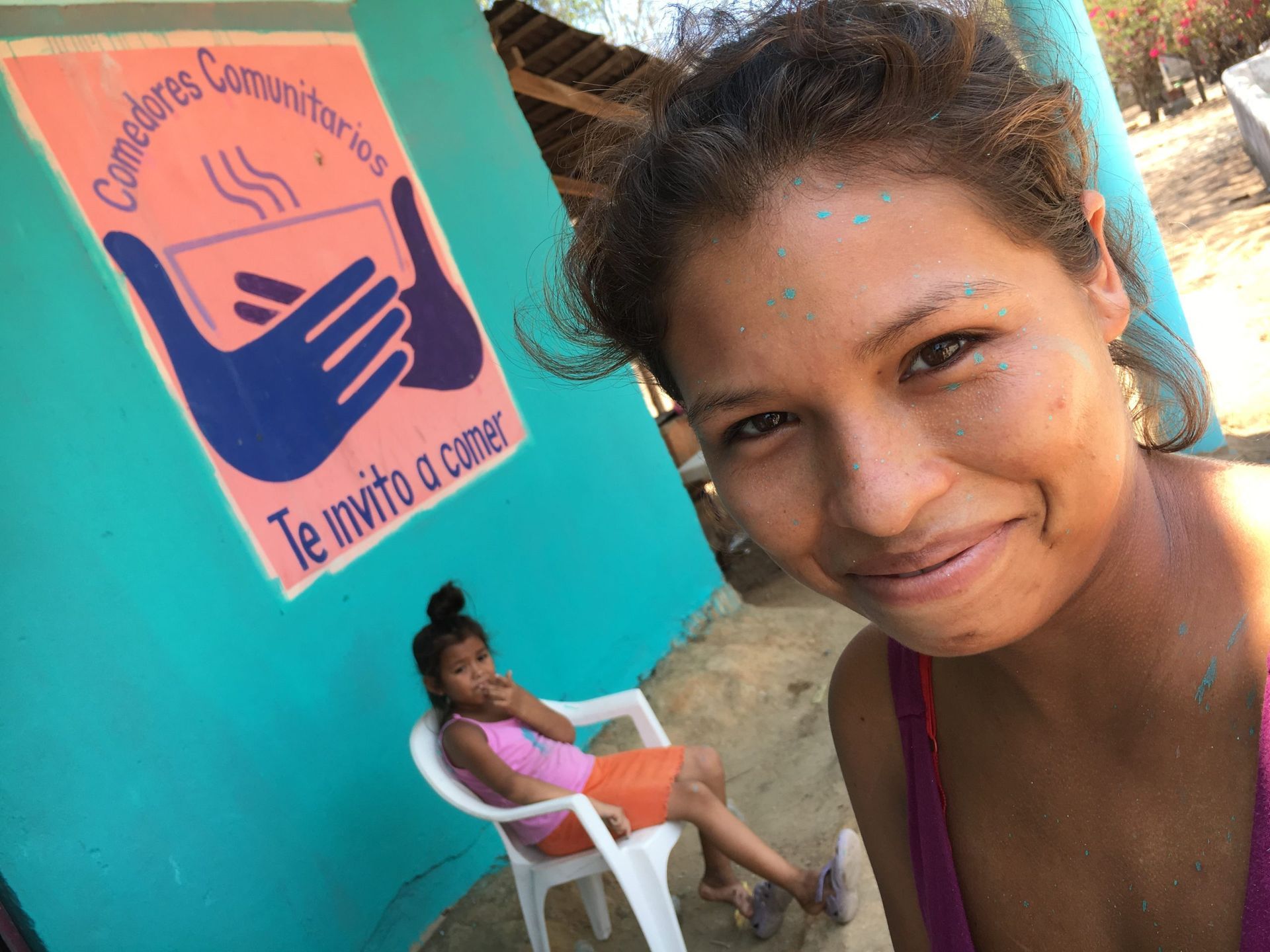 Woman smiling for selfie beside teal wall with health sign and seated person on white chair