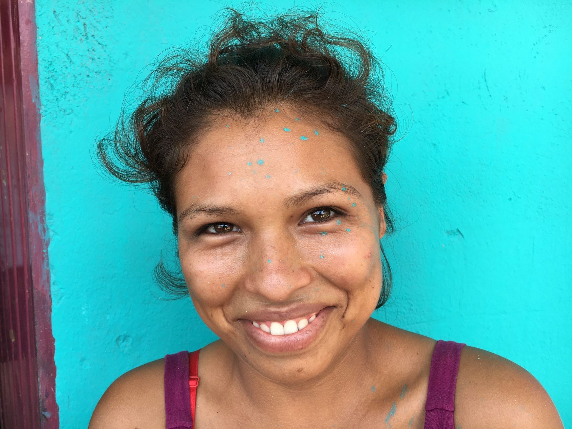 Smiling person in a purple top against a turquoise wall