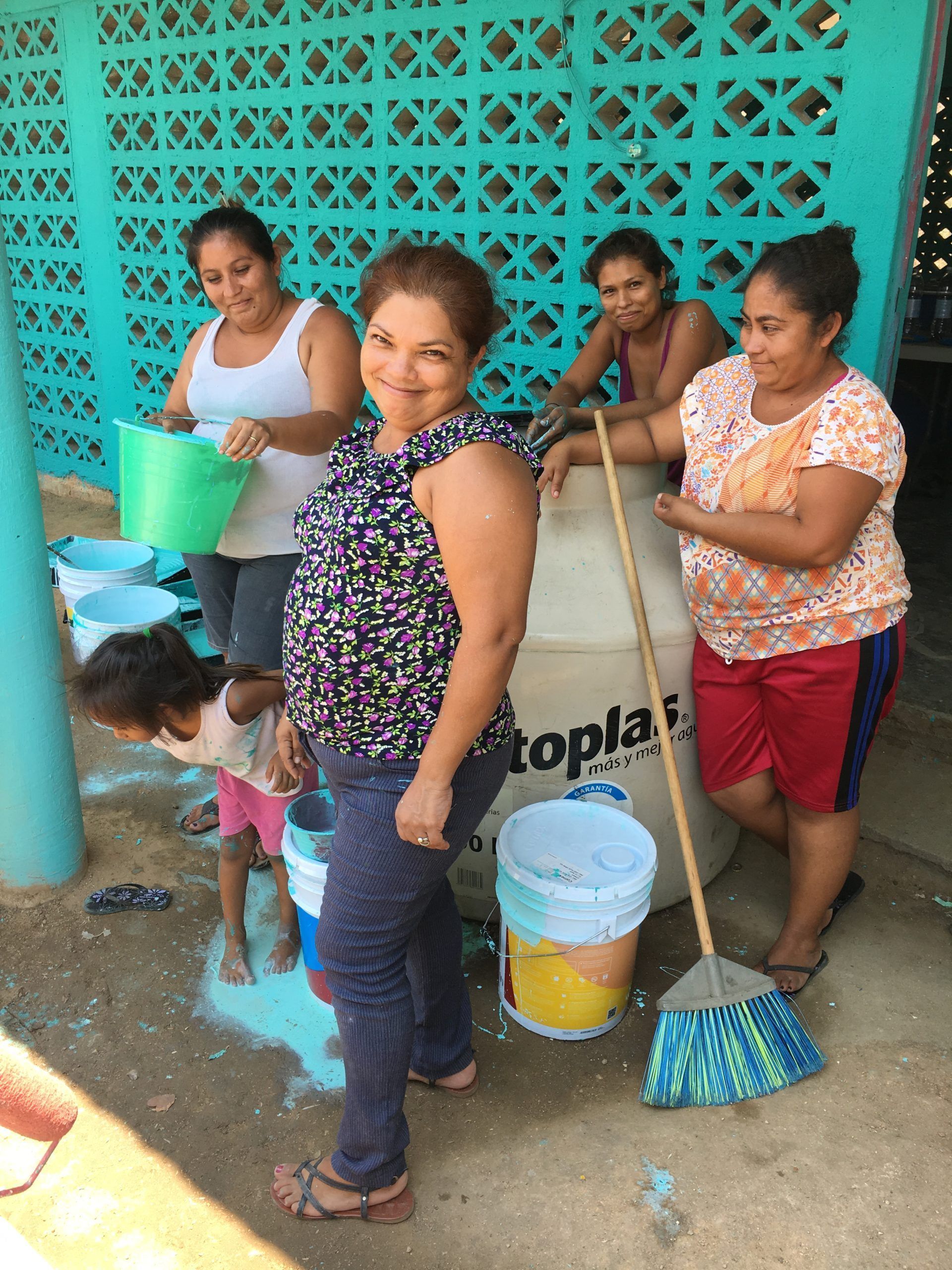 Four women with brooms and buckets cleaning outside a turquoise wall