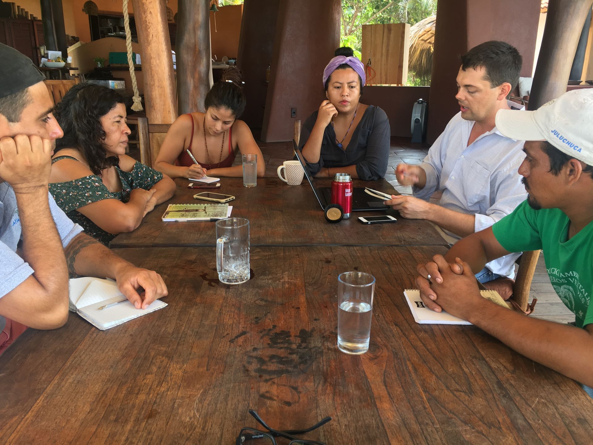 Group seated around a wooden table in a rustic room, talking over drinks and notepads.
