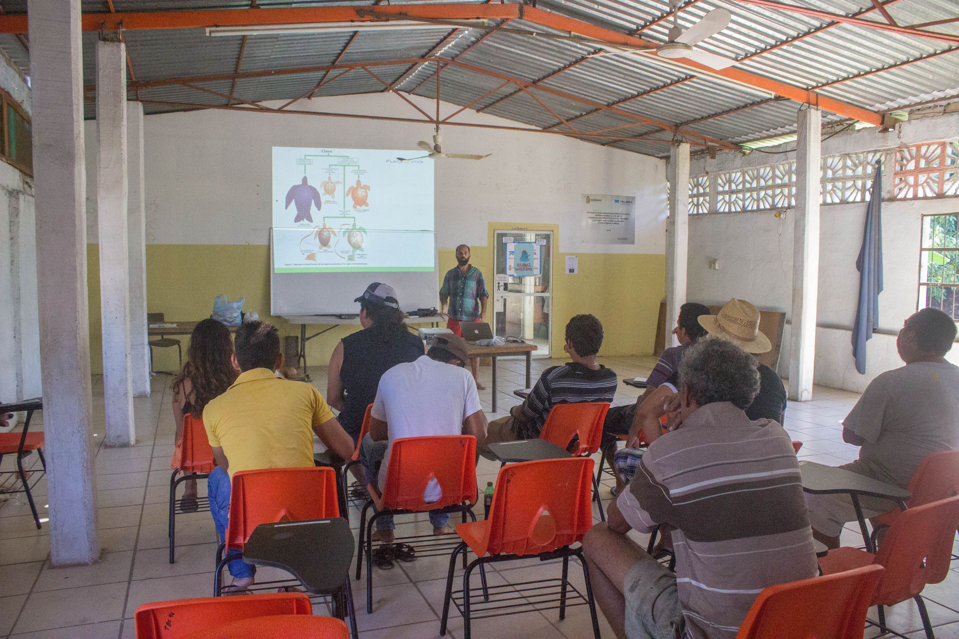 People seated in a hall watching a presentation projected on a screen.