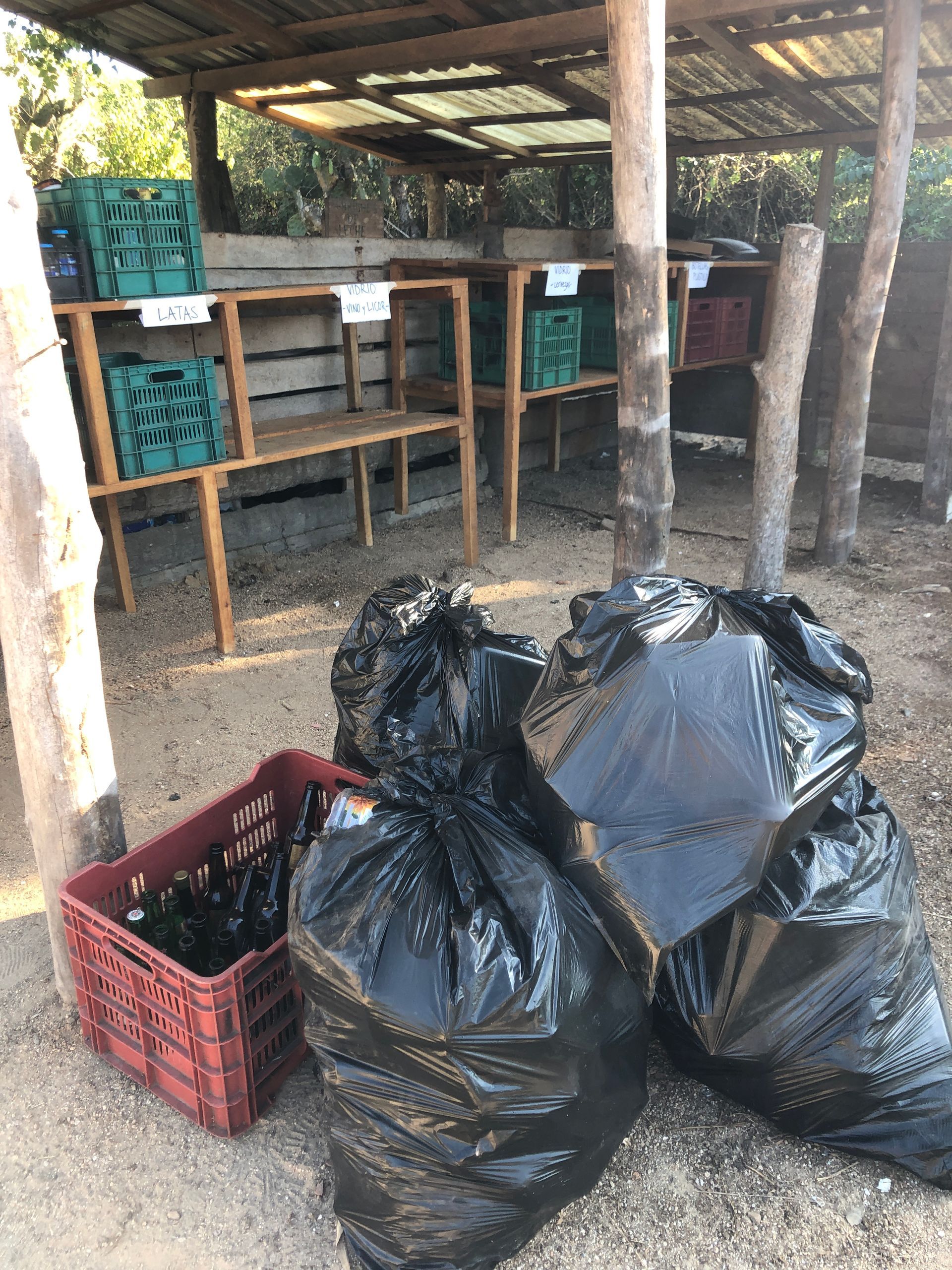 Black garbage bags and a red crate in a rustic open shed with wooden tables and posts.