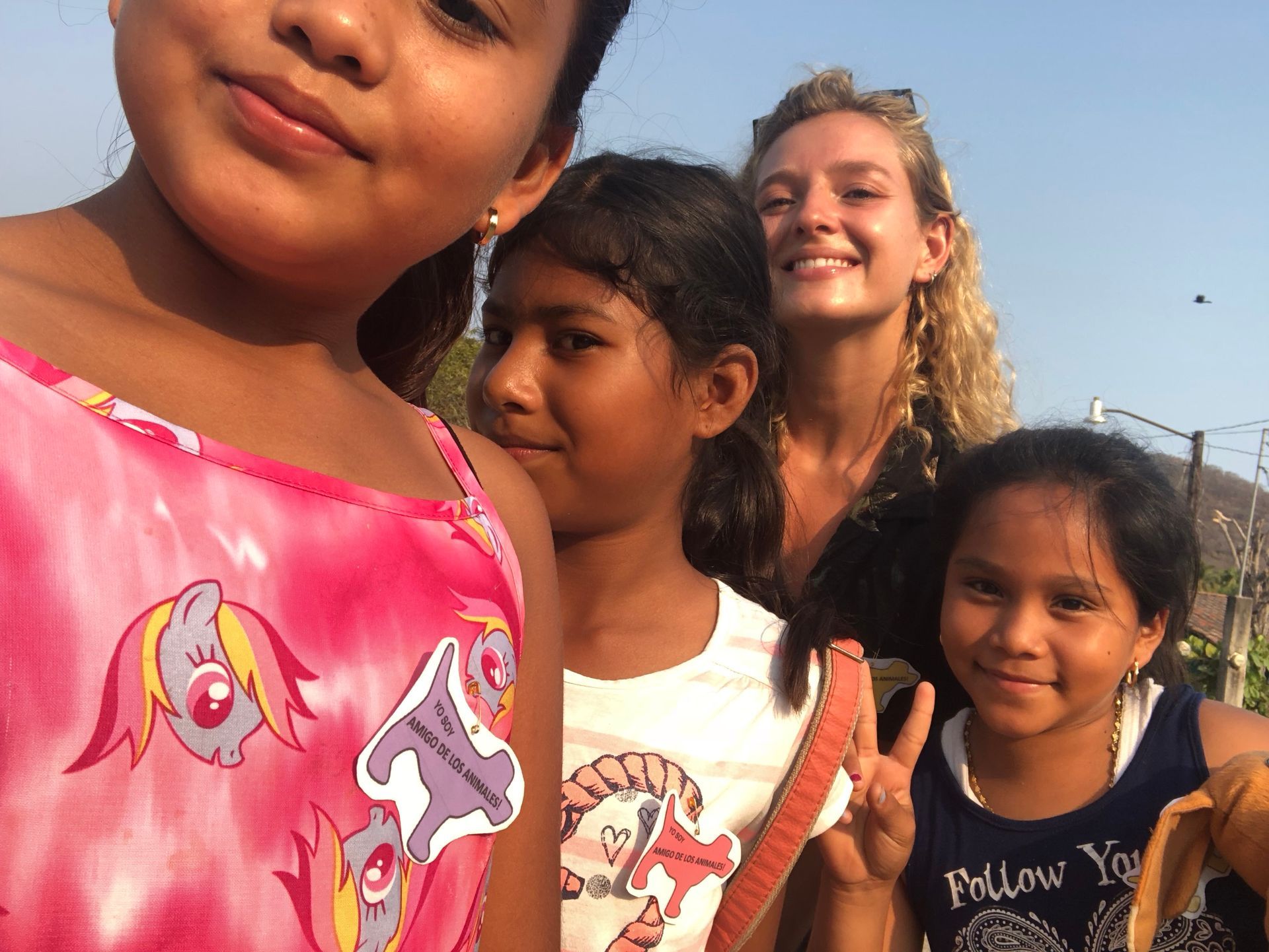 Four people smiling outdoors under a blue sky, with one child close to the camera in a pink shirt