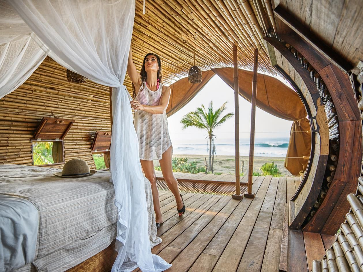 Woman standing in a rustic beachfront hut with draped white canopy and ocean view