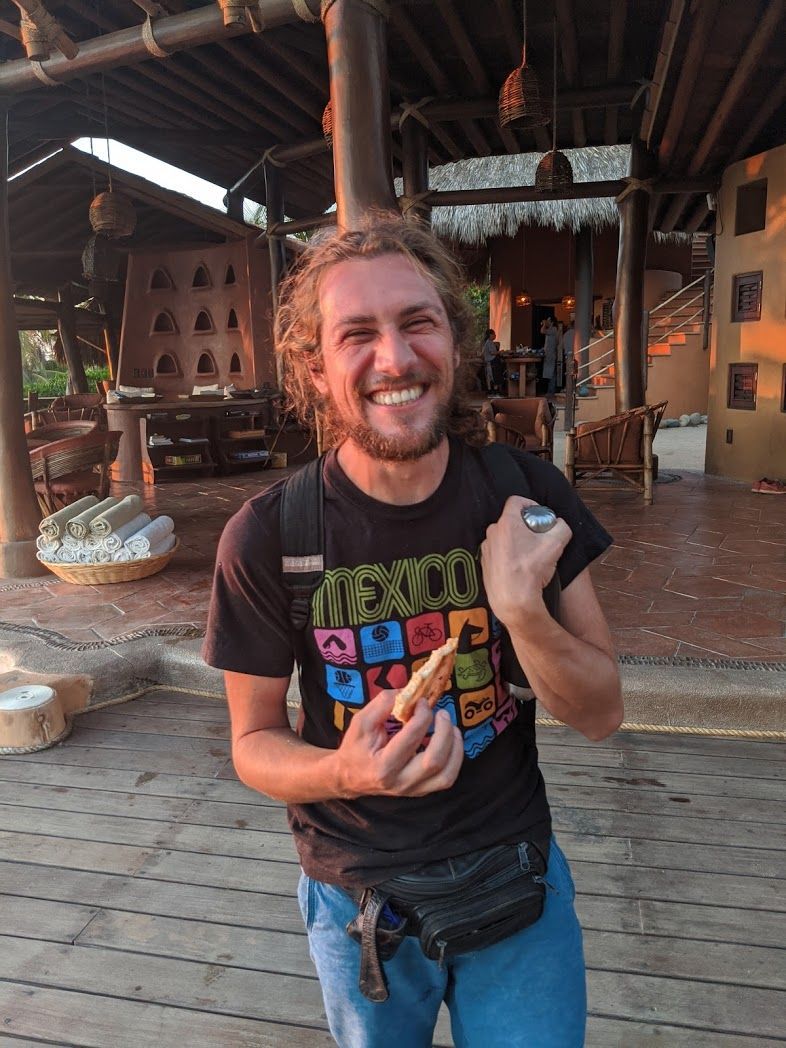 Smiling person in a black graphic T-shirt holding a snack inside a rustic wooden shop
