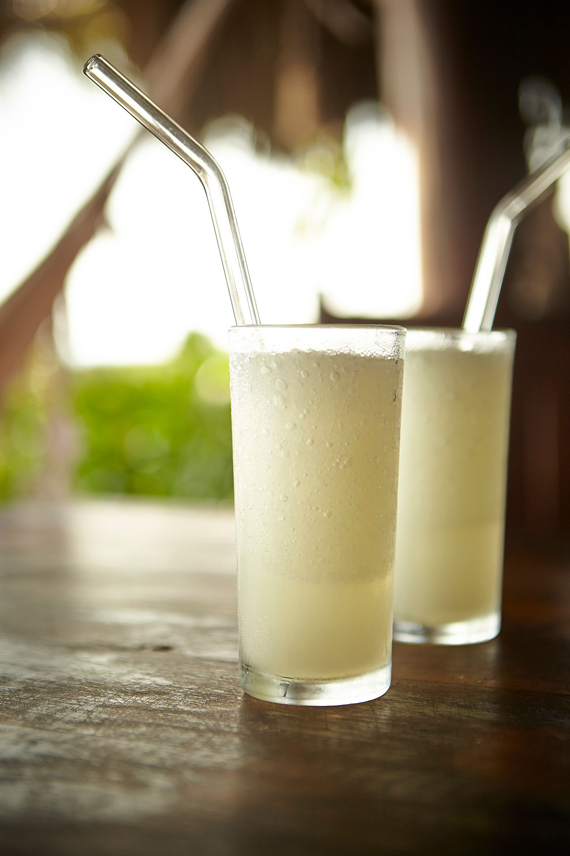 Two frothy drinks with metal straws on a wooden table, softly lit with a blurred background
