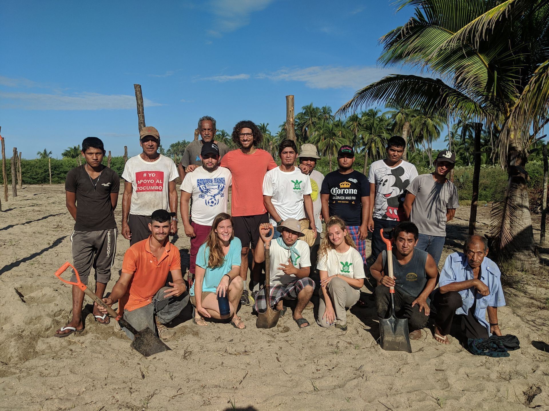 Group of people posing on a sandy beach with palm trees and blue sky in the background